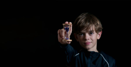 Portrait image of a boy with an hourglass on a dark background