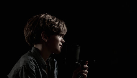Portrait of a little boy with long hair singing near a microphone on a dark backgroundの写真素材