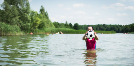 Young girl swimming and playing in the lake with a ballの写真素材