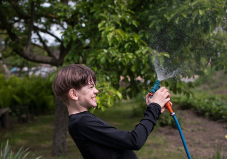 Portrait of a teenage boy in the garden playing with water in a country houseの写真素材