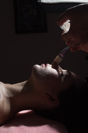 Spa concept. Young woman with nutrient facial mask in beauty salon, close up. low key photoの写真素材