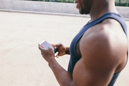 Portrait of serious busy African entrepreneur in shirt and glasses, using mobile phone for business correspondence, looking at the screen with concentrated face. Selective focus on the cell phoneの写真素材