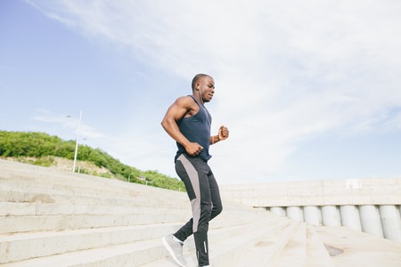 male african athlete running up flight of stairs with speed, training or working out outdoors while jogging up stepsの写真素材