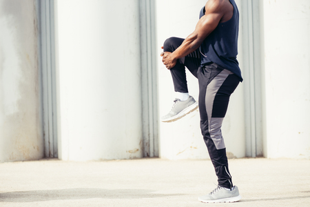 Image of muscular young man working out against sky. African man looking away with stretching his leg. Shirtless male model exercising outdoors.の写真素材