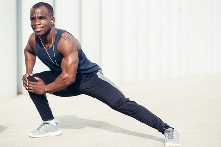 Black man doing stretching before running in urban background. Young male exercising listening to music with headphones.の写真素材