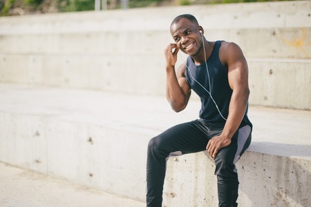 Young cute African American sportsman or jogger contemplating beauty of new day. Attractive black man admiring sunrise listening to music in his earphones, meditating, looking far away, dreamingの写真素材