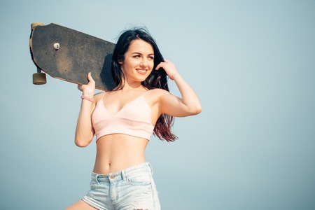 Portrait of Beautiful young adult woman standing with skateboard on shoulderの写真素材