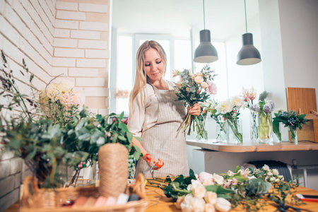 Florist workplace: woman arranging a bouquet with roses, matthiolas, ranunculus flowers and gypsophila paniculata twigs.の写真素材