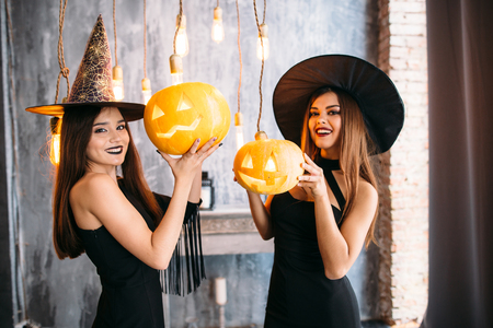 Two cheerful young women in witch halloween costumes with pumpkinsの写真素材