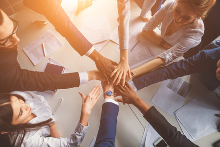 Close-up of people holding hands together while sitting around the desk