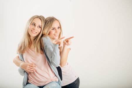 Two cheerful attrative sisters twins pointing over white backgroundの写真素材