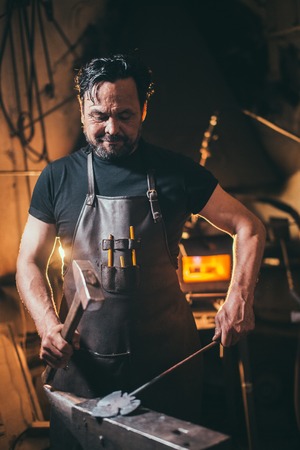 blacksmith manually forging molten metal on anvil in smithy with spark fireworksの写真素材