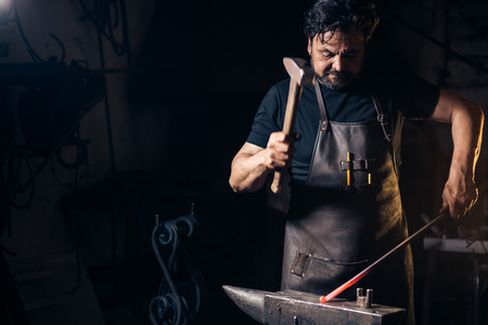 Senior blacksmith forging molten metal on the anvil in smithy.の写真素材