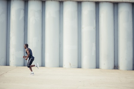 Attractive fit man running fast at sunset light, black man doing workout outdoorの写真素材