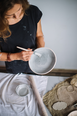 Pretty young woman potter paints a clay cup. Woman working In her pottery studioの写真素材