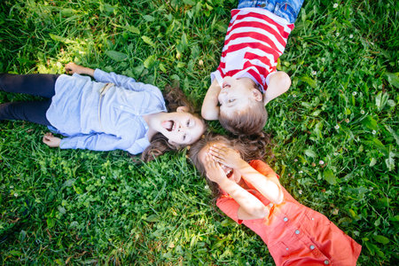 Group of happy cheerful beautiful children lying on grass in park, outdoor