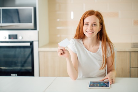 Woman smiling, using tablet screen and holding credit card in living roomの写真素材