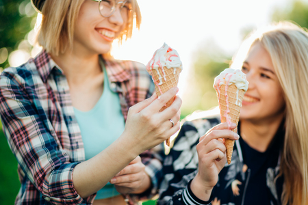 Two best friends having ice cream and laughing together outdoorsの写真素材