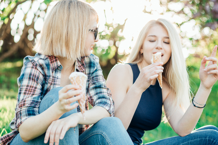 Two best friends having ice cream and laughing together outdoorsの写真素材