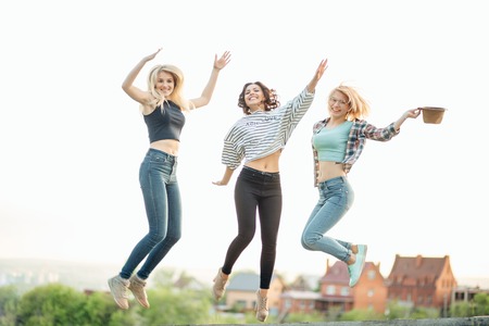 three happy joyful young women jumping and laughing together at parkの写真素材