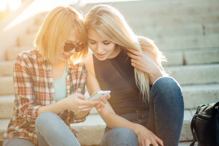 Two beautiful students watching media content on line in smart phone in parkの写真素材