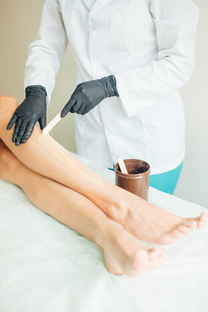 close up Young woman waxing her client lower leg