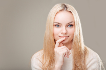 smiling flirting woman with long curly hair and finger on lipの写真素材