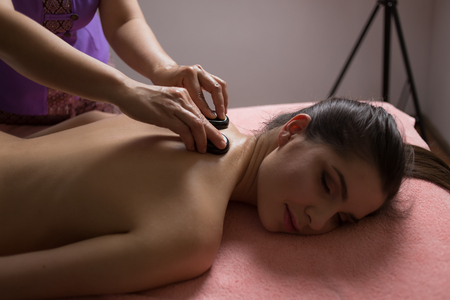 massage therapist putting spa stones on the back of girl lying on massage tableの写真素材