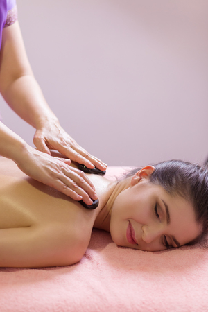 massage therapist putting spa stones on the back of girl lying on massage tableの写真素材