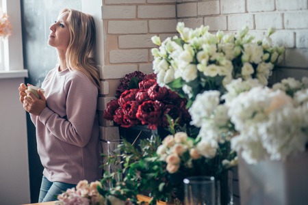 Florist woman in process of making bouquet, holds in her hand a cup of coffeeの写真素材