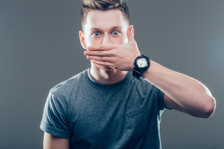 Shocked man covering mouth with hand and looking awayの写真素材