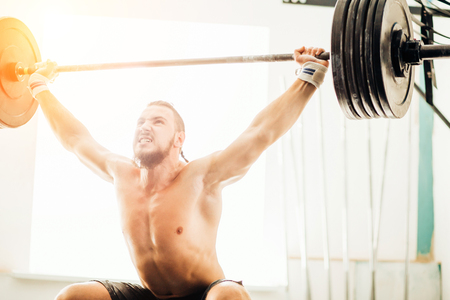 brutal muscular man with beard train with barbell raised over head in gymの写真素材