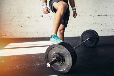 young man preparing for barbell training in gym. put his leg on barbellの写真素材