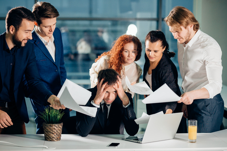 Businessman holding head with hands surrounded by colleagues with documentsの写真素材