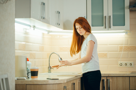 woman pouring water from faucet into glass in kitchenの写真素材