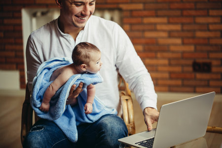 man working at desk at home with laptop, holding cute babys, looking at screen