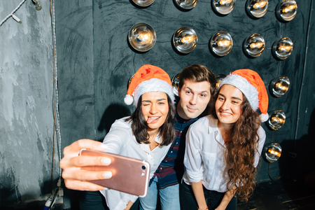 girls and guys in Santa hats doing selfie at party. Christmas, new year conceptの写真素材