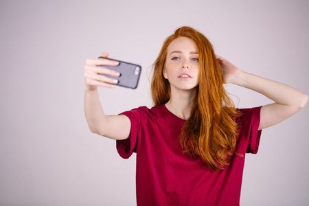 redhead girl takes a selfie. She has long red hair. wears marsala t-shirtの写真素材