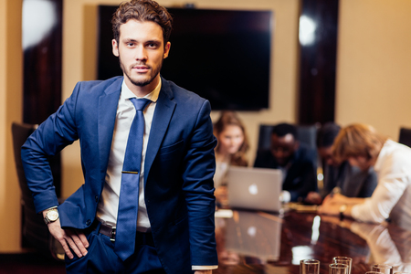 businessman looking at camera with blurred workers on backgroundの写真素材
