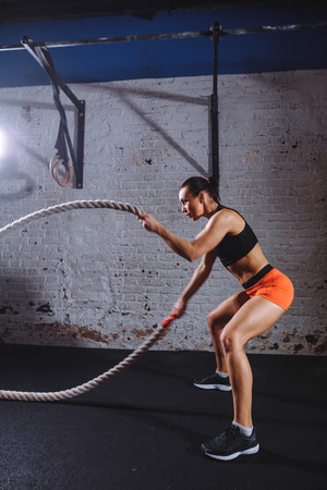 athletic woman doing some cross fit exercises with battle rope indoorの写真素材
