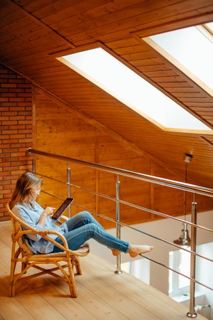 woman at home sitting on modern chair relaxing in room using tabletの写真素材