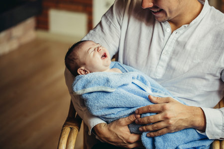 Father With Newborn Baby Working From Home Using Laptop