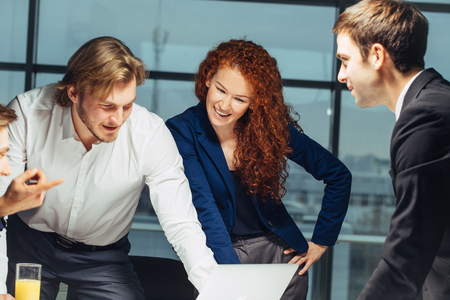 Smiling Female And Handsome Male Co-Workers Sitting At Table, Looking At Laptopの写真素材