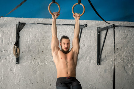 Muscle-up exercise athletic man doing intense workout at gym on gymnastic rings