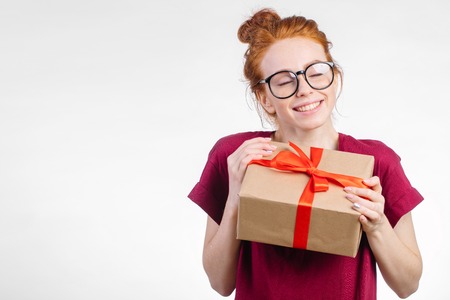 Happy redhead woman in glasses holding gift box on white backgroundの写真素材