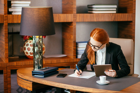 woman writing on paper with digital tablet computer in office roomの写真素材