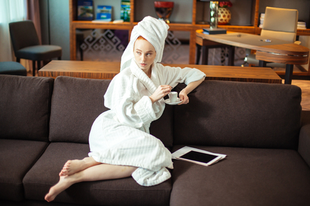 young woman in bathrobe drinking coffee and reading on digital tabletの写真素材