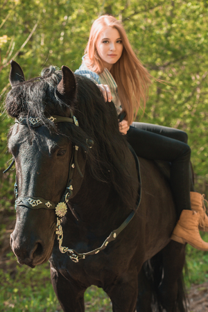 brunette woman wearing white dress riding dark horse at summer green forestの写真素材