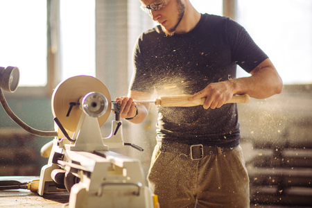man working at small wood lathe, an artisan carves piece of woodの写真素材
