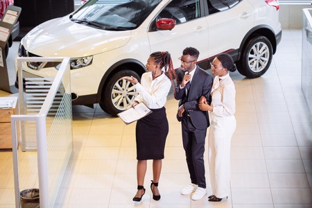 car salesman standing at dealership telling about features of car to customersの写真素材